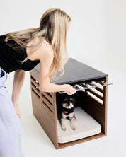 Person opening a modern wooden pet bed with a dog inside on a white background