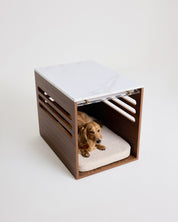Dog lying on a cushion inside a modern wooden pet bed with marble top.